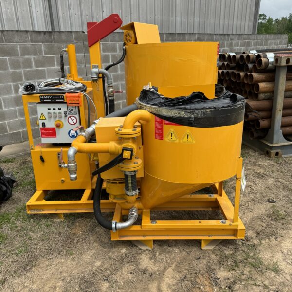 1743642058016919189_tempImage - Big River Trenchless & GeoServices Yellow industrial machinery with control panel and hoses on a metal frame outdoors near a cinder-block wall; stacked pipes to the right.