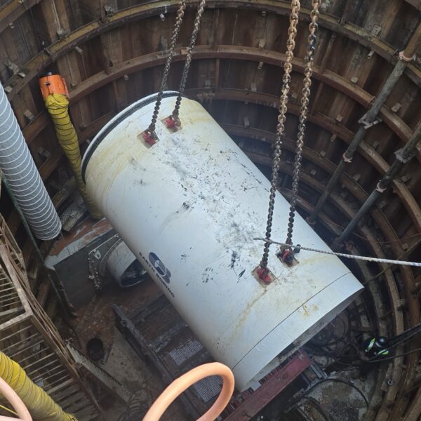 1783000959201686768_tempImage - Big River Trenchless & GeoServices Large white cylindrical tank being lowered by chains into a deep circular industrial shaft.