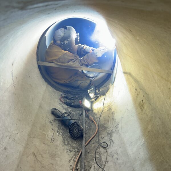 75EC10D5-556F-4C23-BC73-A49BC3C34A2B - Big River Trenchless & GeoServices Worker in protective suit and helmet welding inside a circular concrete tunnel.
