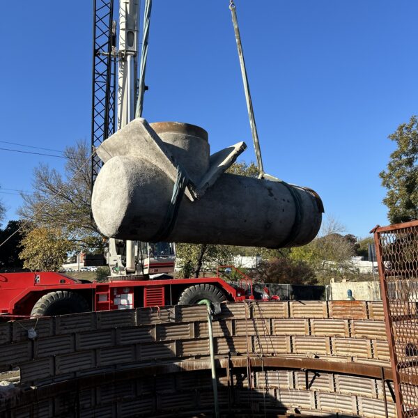 9929F946-72DD-4146-AF0D-CBC489F4FFD1 - Big River Trenchless & GeoServices Crane lifting a large concrete pipe over a trench at a construction site.