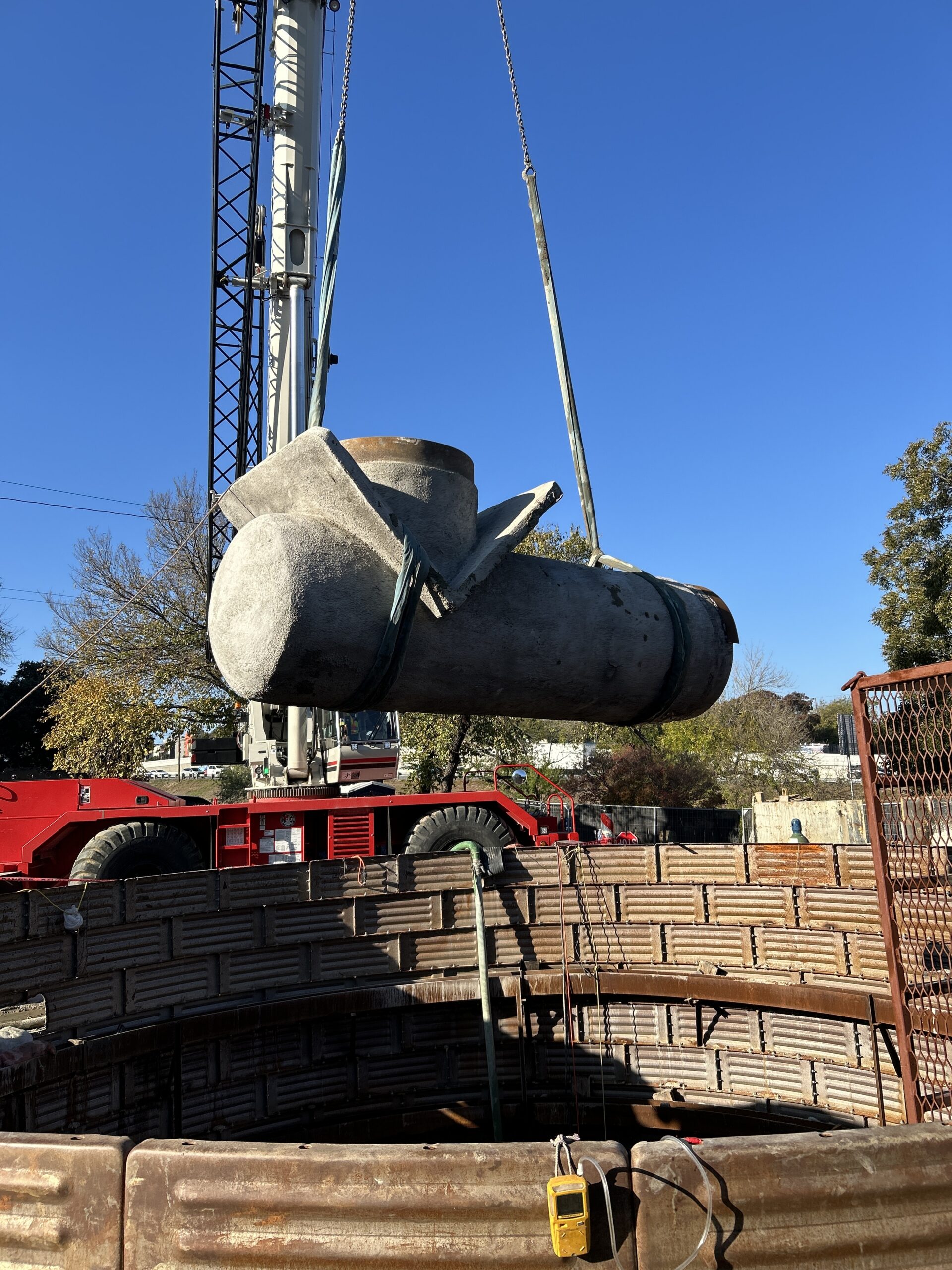Crane lifting a large concrete pipe over a trench at a construction site.