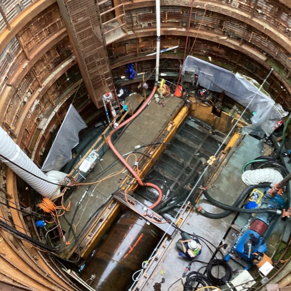 9FF77D58-710D-4B9D-89E5-EA56E8464EED - Big River Trenchless & GeoServices Deep circular underground shaft under construction with metal rings, scaffolding, and scattered tools/hoses.
