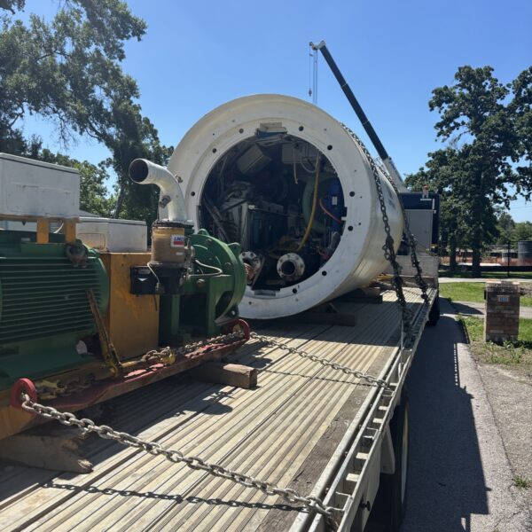 B573E48F-7E1F-4C0B-BD3F-DD4840CD2473 - Big River Trenchless & GeoServices Large cylindrical industrial machine mounted on a flatbed trailer, with a crane and greenery in the background