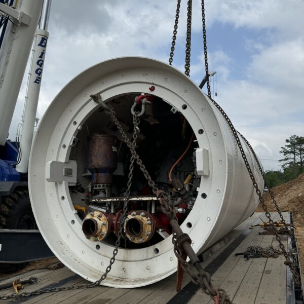 C5C1E3C0-BD75-4EDA-9746-E59C97351CAD - Big River Trenchless & GeoServices Large industrial cylindrical machine being lowered or installed, with heavy chains and a crane hook visible on a flatbed trailer.