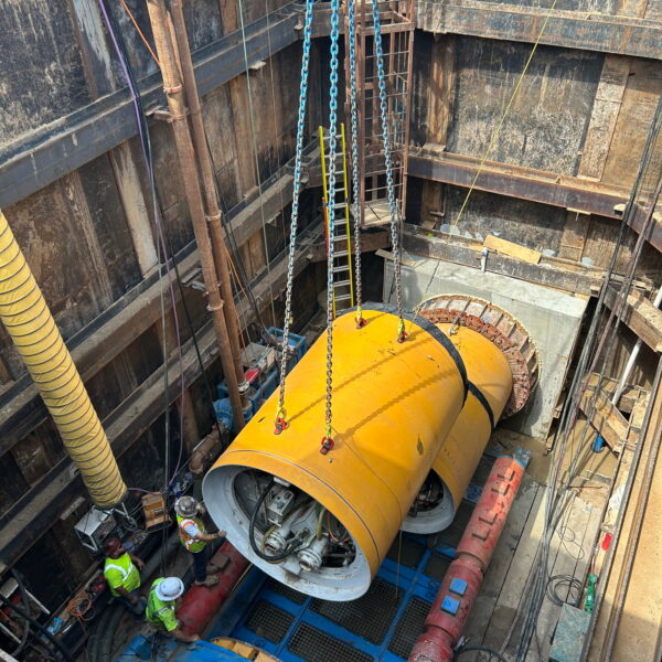 ZacateCreekWWTP-Img12 - Big River Trenchless & GeoServices Yellow industrial turbine housing being lowered into a deep excavation by multiple chains, with workers in hard hats nearby.