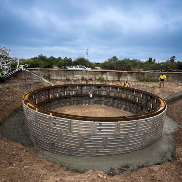 ZacateCreekWWTP-Img2 - Big River Trenchless & GeoServices Large circular metal formwork ring set in dirt at a construction site, with workers in high-visibility vests nearby.