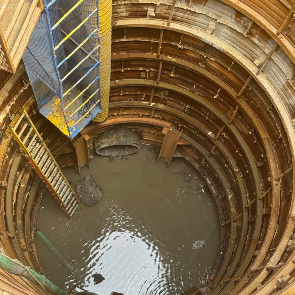 ZacateCreekWWTP-Img3 - Big River Trenchless & GeoServices Deep circular excavation shaft with rusted metal rings, scaffolding and a yellow duct hanging inside, water gathered at the bottom.