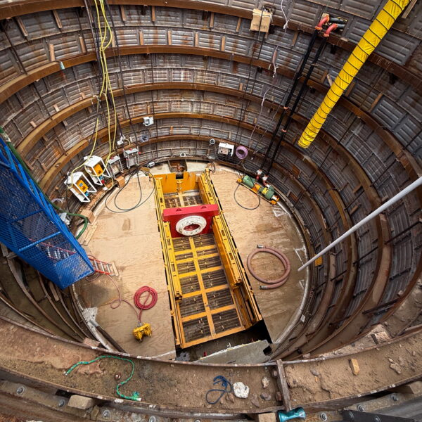 ZacateCreekWWTP-Img4 - Big River Trenchless & GeoServices Inside a deep circular underground shaft under construction, with concentric metal rings, suspended hoses, and a orange-yellow work platform at the bottom.