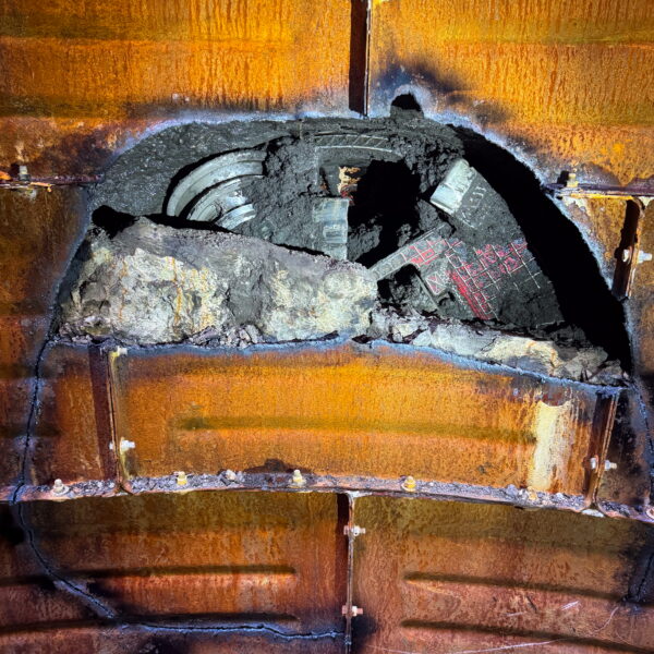ZacateCreekWWTP-Img9 - Big River Trenchless & GeoServices Rusted, orange-brown metal interior with a large cracked opening filled with charred coal and ash at the center.