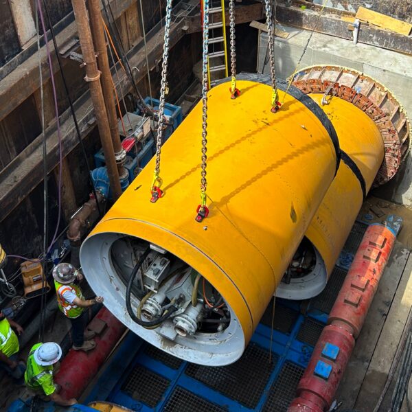 HPaboutus-Img - Big River Trenchless & GeoServices Large yellow industrial cylinder being lowered into a shaft with heavy chains, surrounded by scaffolding and workers in safety vests and helmets.