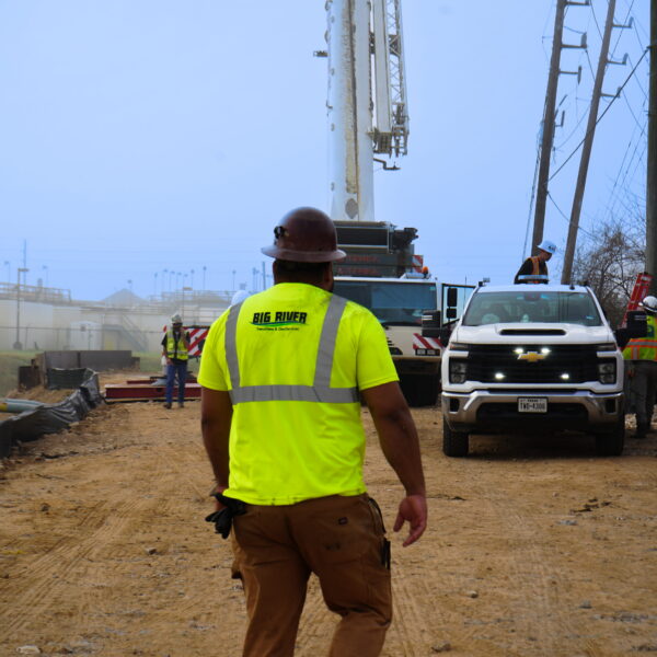 WHCRWA-Contract-64-Img1 - Big River Trenchless & GeoServices Construction crew at a worksite with a white truck, power lines, and a tall equipment tower in the background; worker in a neon yellow vest in foreground.