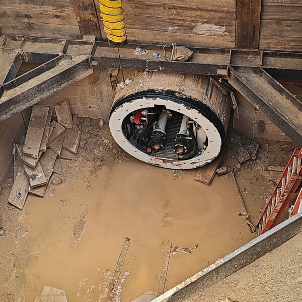 WHCRWA-Contract-64-Img13 - Big River Trenchless & GeoServices Construction site trench with a large circular manhole frame in muddy water, surrounded by wooden formwork and a yellow duct.