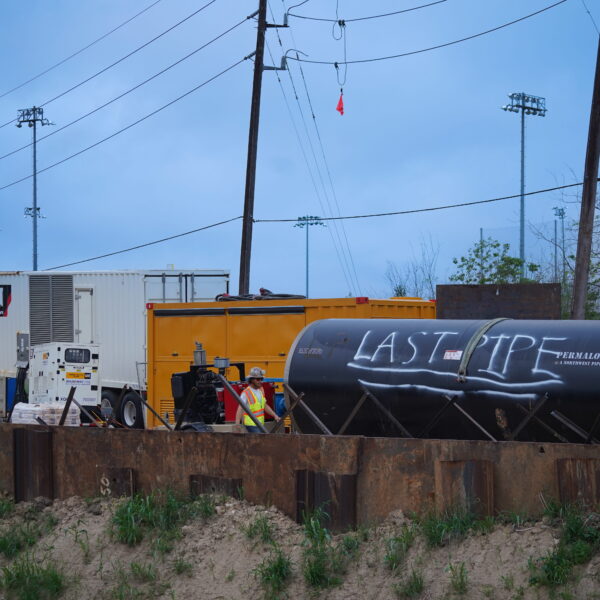 WHCRWA-Contract-64-Img16 - Big River Trenchless & GeoServices Construction site with a large black pipe/container labeled 'LAST PIPE', yellow equipment, and a worker in a reflective vest nearby.