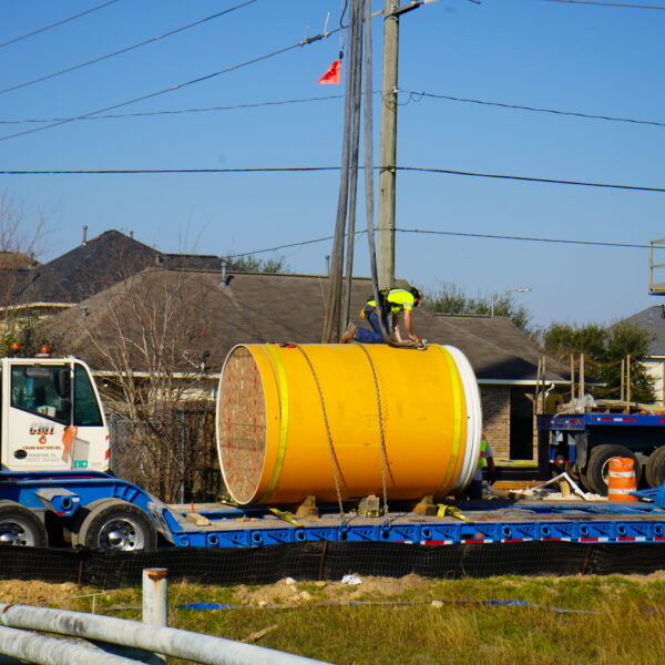 WHCRWA-Contract-64-Img4 - Big River Trenchless & GeoServices Construction site with a worker in a neon vest kneeling on a large yellow cylindrical pipe on a blue trailer area